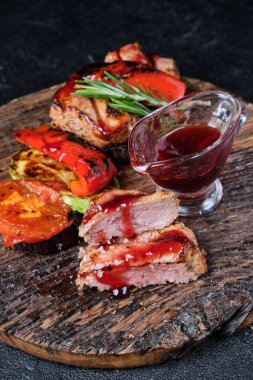 Kesme tahtasında ızgara dana eti ve ızgara sebze ve koyu beton arka planda kiraz sosu.