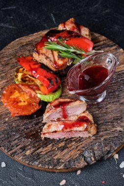 Kesme tahtasında ızgara dana eti ve ızgara sebze ve koyu beton arka planda kiraz sosu.