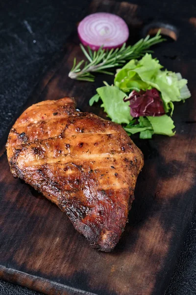 Grilled chicken fillets on wooden cutting board. Black concrete background