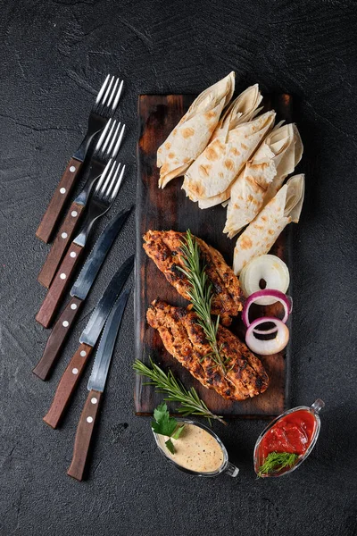 Izgara et şişi, şiş kebap ve pide kesim tahtası ve çatal bıçak takımı, iki sos, soğan. Siyah arka planda, en üstte. Gürcistan mutfağı kavramı. Et ve baharattan yapılmış sulu lula kebabı.