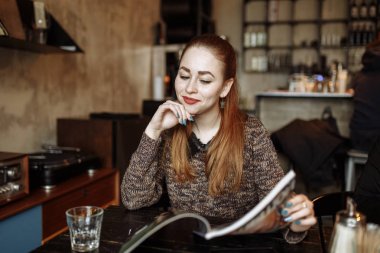 Kafede masada oturan ve dergi okuma güzel genç kadın