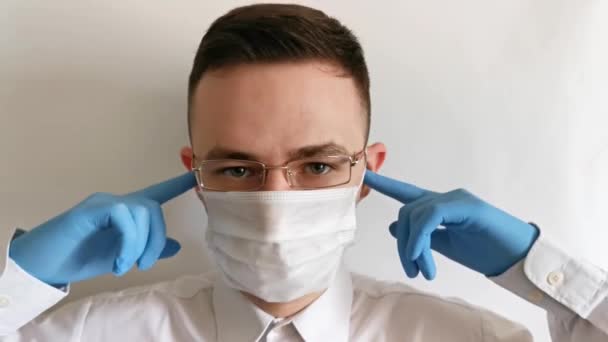 Un hombre con guantes, una máscara y gafas agita su cabeza sobre un fondo claro — Vídeos de Stock