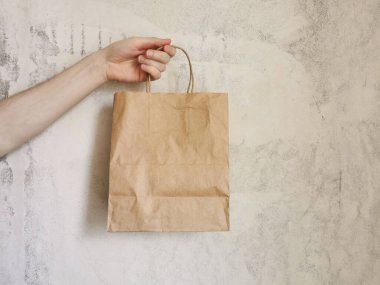 Bej arka planda eko paket. Bir adam el çantası tutuyor. Teslimat hizmeti konsepti. Paketleme şablonu modeli. Mesaj için yer var. Reklamcılık.