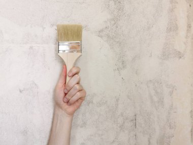Elindeki boya fırçası. Bej arka plan. Apartmanda tamirat var. Metin için yer.