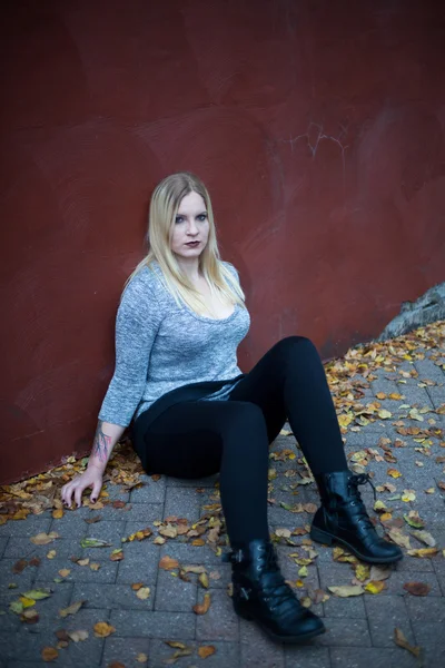 Sonbaharda bir duvarın önünde oturan genç sarışın