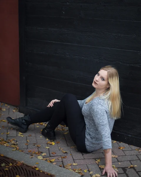 Raslantı giyimli genç kadın bir duvarın önünde oturan