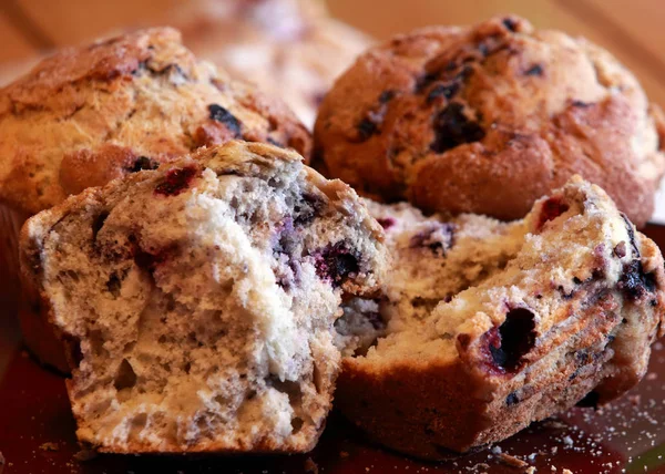 Alan sığ derinliği ile bir meşe ahşap masada üç büyük berry kekler. Biri açık ve yemeye hazır kırık. Ön plana odaklanın. 