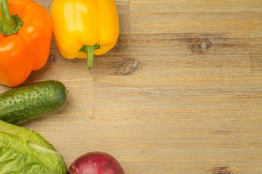 Sebze etrafındaki ahşap masa arka plan üzerinde. Salatalık, yeşillik, kesme tahtası, biber portakal ve sarı, kırmızı soğan. Vegan veya vejetaryen. Sağlıklı beslenme. Salata.