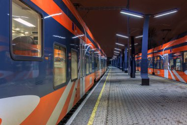 Tallinn Estonya - 22nd Kasım 2016: Yeni modern turuncu tren platformu üzerinde duran hiç kimse gece, boş istasyonunda. Koyu, iki aktarım her iki taraf ışıklar.