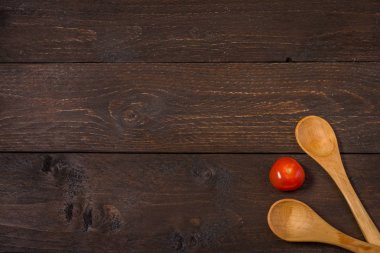 Two wooden spoons on a dark wood background and vegetables red cherry tomatoe vitamins delicious in the middle. Vegeterian or vegan background. clipart