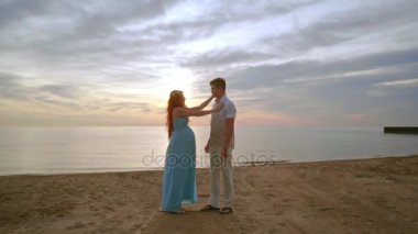 Hamile çift üzerinde gündoğumu kumsalda. Erkek ve kadın deniz plaj