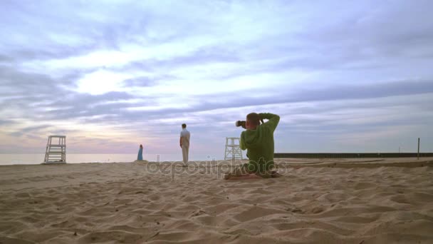 Фотограф фотографирует пару на пляже. Романтическая фотосессия — стоковое видео