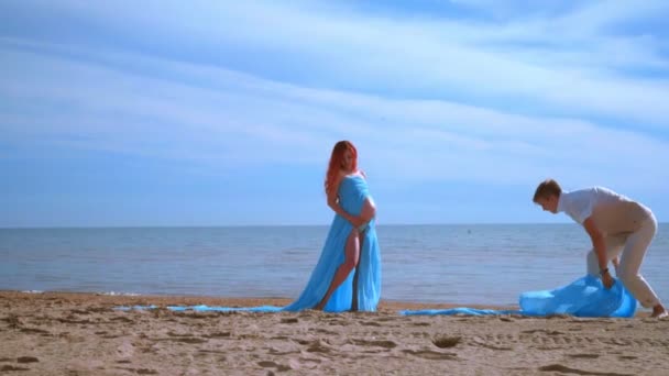 Zwangere vrouw op strand zee. Blauwe doek vliegen in de wind op het strand — Stockvideo