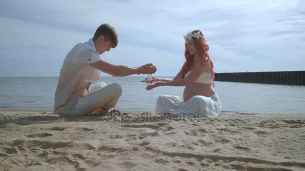 Zwangere paar ontspannen op het strand. Gelukkige paar gieten zand in handen op strand — Stockvideo