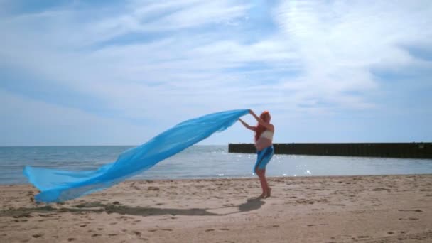 Mujer embarazada divirtiéndose con tela azul volando en el viento. Playa de mujer embarazada — Vídeo de stock