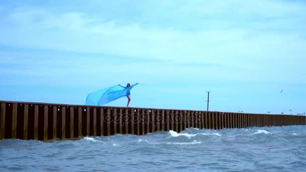 Жінка в літаючому одязі на морському пірсі. Жінка летить у вітрі. Романтична концепція — стокове відео