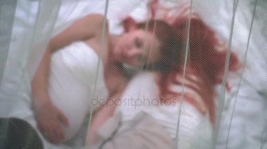 Beyaz kumaş üzerine saydam perde yatan kızıl saçlı kadın