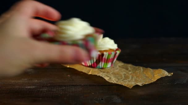 Muffins con crema de pastel sobre papel para hornear. Mano poner magdalena en la mesa — Vídeos de Stock