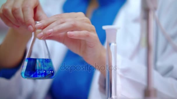 Wetenschappelijk laboratoriumonderzoek. Vrouwelijke wetenschapper handen mengen blauwe vloeistof in de kolf — Stockvideo
