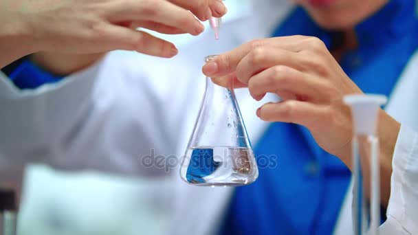 Primer plano de las manos del investigador de laboratorio goteando líquido puro en el frasco de laboratorio — Vídeos de Stock