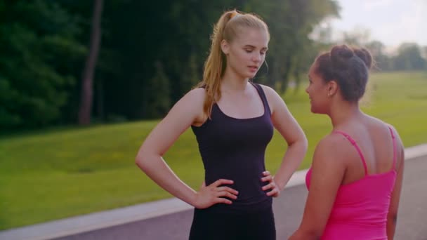 Mulattin im Gespräch mit blondem Mädchen. Freundinnen unterhalten sich im Sommer im Park — Stockvideo