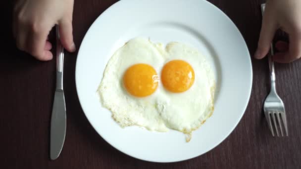 Жареные яйца едят. Вид сверху на жареные яйца, поедающие вилкой и ножом — стоковое видео