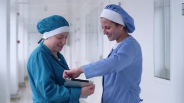 İki kadın tablet beyaz koridorda kullanma. Tablet seyir ve gülümseyen laboratuvar kadınlar