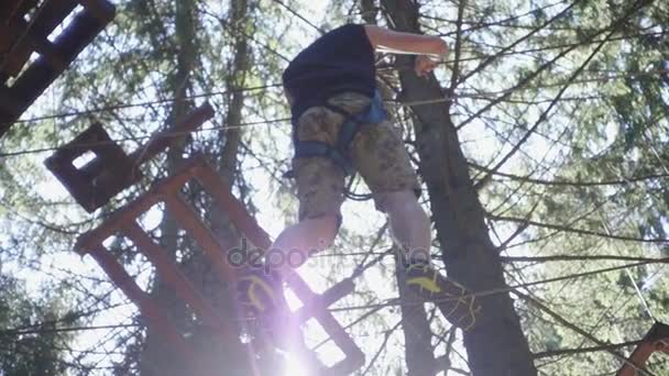 Ung man i säkerhetsutrustning som går på repet på hög i sommar klättring park — Stockvideo
