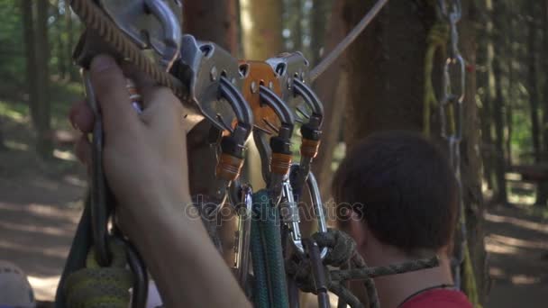 Мужчина берет карабин с веревкой для экстремального восхождения на дерево в парке приключений — стоковое видео