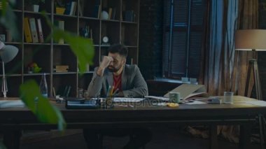 Ev stüdyosunda iş gününün sonunda yorgun iş adamı. Masa başında oturan yorgun adam
