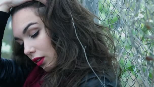 Portrét ženy dotýká vlasů a při pohledu kamery na plotové pletivo pozadí — Stock video
