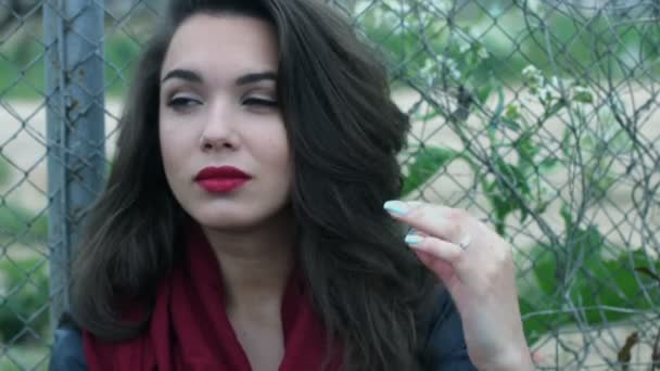 Portrait attrayant femme touchant de longs cheveux bruns sur fond de maille de clôture . — Video