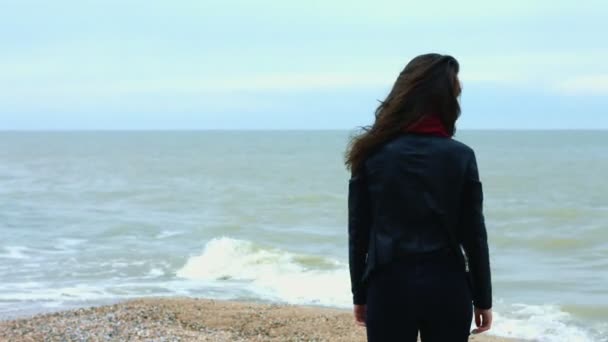 Jonge vrouw aanraken brunette haar bewegen op wind tijdens het wandelen aan zandstrand — Stockvideo