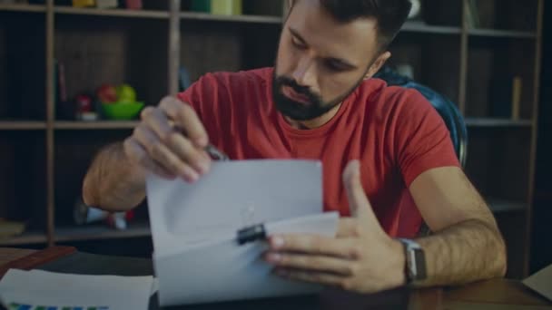 Joven hombre de negocios que trabaja con pluma con documentos comerciales en la oficina por la noche — Vídeo de stock