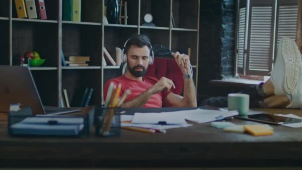 Dueño de una pequeña empresa descansando después de la jornada laboral. Hombre escuchando música en el lugar de trabajo — Vídeo de stock