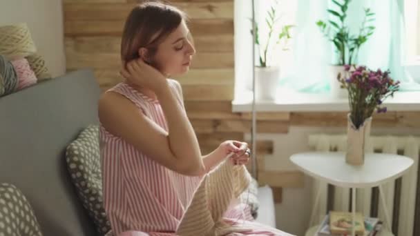 Mujer artesanal tejiendo lana sentada en el sofá en la habitación en la ventana de fondo — Vídeos de Stock