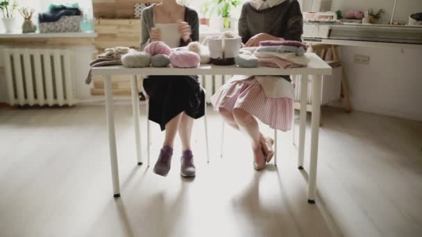 Patas femeninas sentadas a la mesa y agujas de tejer. Mujer tejedora — Vídeo de stock