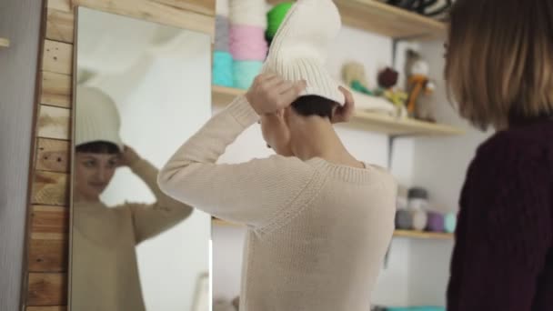 Mujer sonriente vistiendo sombrero de punto y mirando en el espejo en la sala de exposición — Vídeos de Stock