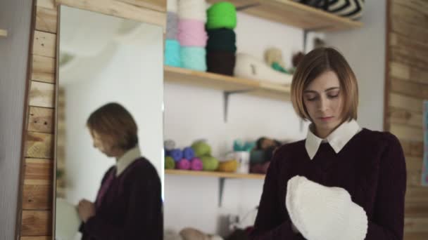 Mujer joven de pie espejo delantero con gorra de punto. Mujer en taller textil — Vídeo de stock