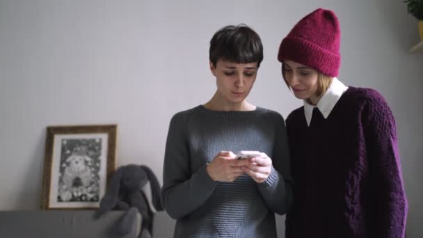 Twee vrouw in stijlvolle trui op zoek foto op smartphone. Vriendinnen gossip — Stockvideo