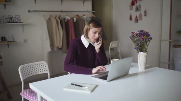 Jeune femme assise à table et parlant par téléphone portable. Femme utilisant un ordinateur portable — Video
