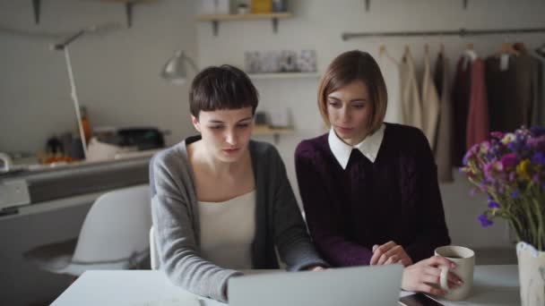 Dos mujeres de negocios trabajando en cuaderno sobre fondo colgando ropa — Vídeos de Stock