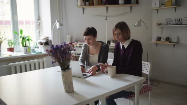 Dos mujeres jóvenes sentadas en la mesa y usando un cuaderno para ordenar en línea — Vídeo de stock