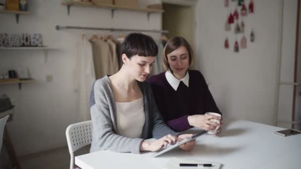 Dvě kreativní žena pomocí tabletu pro nový projekt na pozadí visí oblečení — Stock video