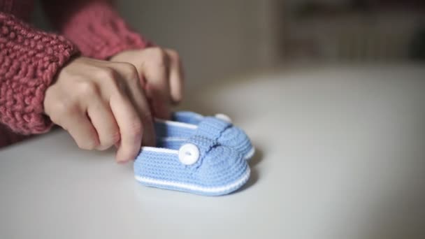 Ženské ruce hrát s pletené dětské botičky. Ručně dělané pro miminko pletené boty