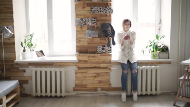 Vacker kvinna med mobiltelefon stående främre fönster i rummet — Stockvideo
