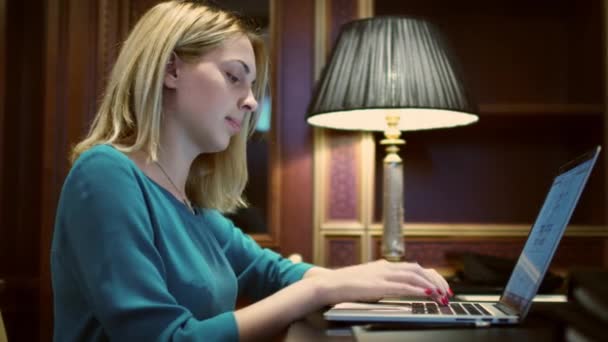 Femme sérieuse ouverture ordinateur portable et dactylographier sur le clavier sur le bureau avec lampe de table — Video