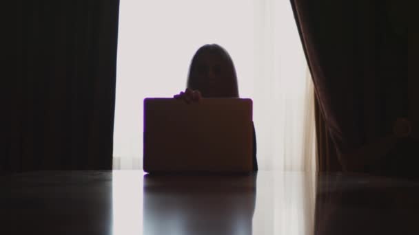 Mujer joven abriendo la computadora portátil sentada en la mesa de nuevo a la ventana — Vídeo de stock