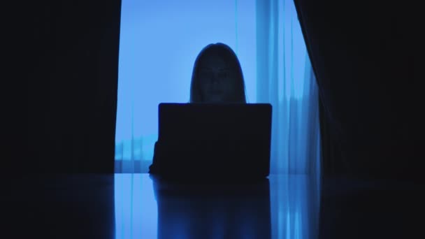 Ділова жінка, що працює на ноутбуці, сидить назад у вікно в темній кімнаті — стокове відео