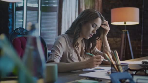 Концентрированная деловая женщина делает заметки за столом с ноутбуком в офисе — стоковое видео
